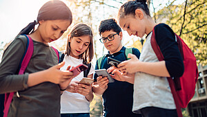 Schulkinder stehen zusammen und benutzen Handys