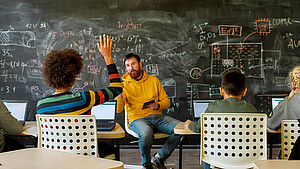 Schüler sitzen im Klassenzimmer vor Laptops und folgen dem Unterricht durch einen Lehrer